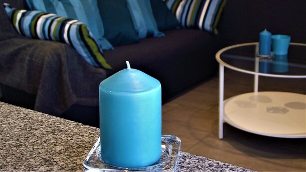 A living room with a blue candle on a glass coaster, a dark-colored sofa with striped cushions, and a small round table with two blue candles. - Playa de Barrañán (Arteixo)