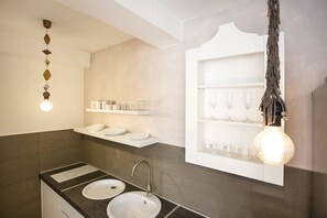 A modern bathroom with two sinks, a mirror, and shelves with glassware.