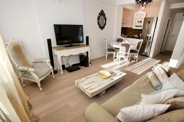 A modern living room with a television, a dining area, and a kitchen in the background.
