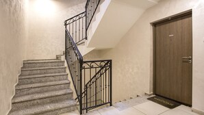 Una escalera con barandilla metálica que lleva a un rellano, una puerta de madera y un felpudo.
