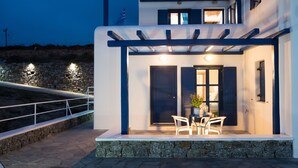 A modern two-story house with a stone exterior, a balcony with white chairs, and a pergola.