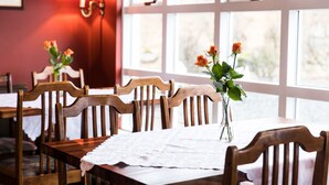 Un coin repas avec des tables et des chaises en bois, un chemin de table en dentelle et un vase rempli de fleurs.