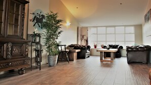 Un salon spacieux doté d’un plancher en bois, d’une grande plante en pot, d’un buffet en bois foncé, d’un canapé en cuir et d’une table à manger.