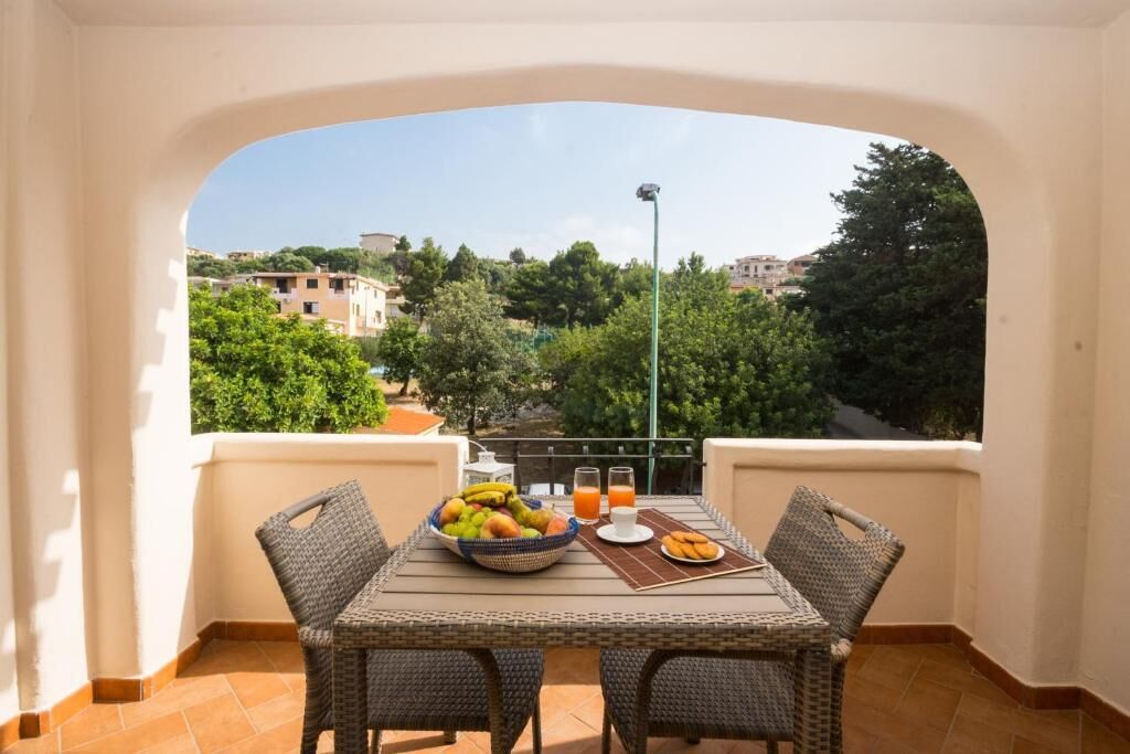 A balcony with wicker furniture, a table with a fruit bowl, a plate of cookies, and a glass of orange juice.