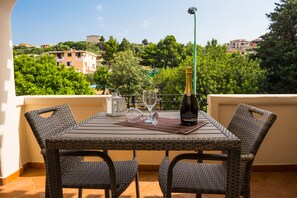 A wicker table with two chairs, a bottle of champagne, and two wine glasses on a balcony overlooking a cityscape. - Micali (Orosei)