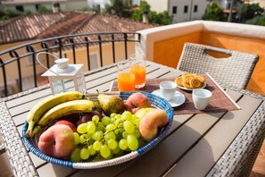 A breakfast setup on a balcony with a wicker table, a fruit basket, a glass of orange juice, croissants, and a cup of coffee. - Micali (Orosei)