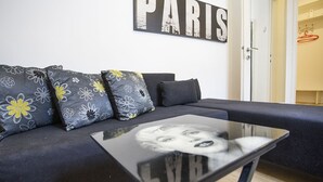 A modern living room with a sofa, floral-patterned cushions, a glass coffee table, and a 'PARIS' sign on the wall. - Apartment Tiffany (Belgrade)