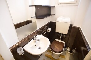 A compact bathroom with a white sink, wooden toilet, and a black shelf above the sink. - Apartment Tiffany (Belgrade)