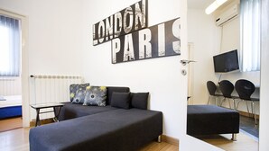 A modern bedroom with a large bed, a small table, a chair, and a TV. There is a wall-mounted sign that reads "LONDON PARIS". - Apartment Tiffany (Belgrade)