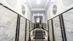 A grand, marble-floored hallway with a central staircase, ornate wall decorations, and a chandelier. - Apartment Tiffany (Belgrade)