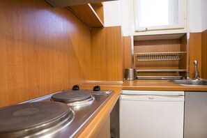 A compact kitchen with wooden cabinets, a built-in stove, a dishwasher, and a metal rack above the sink. - Apartment Tiffany (Belgrade)