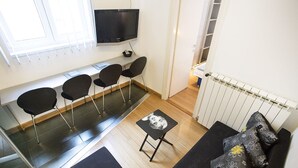 A modern living room with a black sofa, a small black table, and three black chairs. A flat-screen TV is mounted on the wall above the seating area. - Apartment Tiffany (Belgrade)