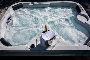 A hot tub with a champagne bottle, two glasses, and a black object on the edge. - Hotel Villa Sandi (Cavle)