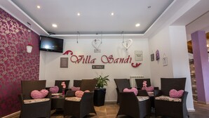 A reception area with wicker chairs, a potted plant, and a wall-mounted TV. - Hotel Villa Sandi (Cavle)