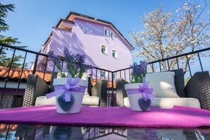 A balcony with wicker furniture and heart-shaped planters with purple ribbons. - Hotel Villa Sandi (Cavle)