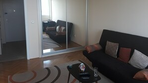 A living room with a black sofa, a coffee table with a remote control, and a glass of water. - Apartment Loti (Belgrade)