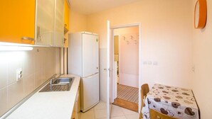 A compact kitchen with a refrigerator, a sink, and a small dining table with a patterned tablecloth. - Apartment Loti (Belgrade)