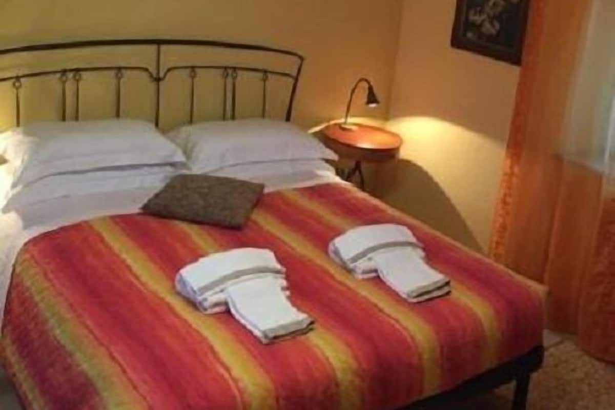 A neatly made bed with a striped blanket, a bedside table with a lamp, and framed pictures on the wall.
