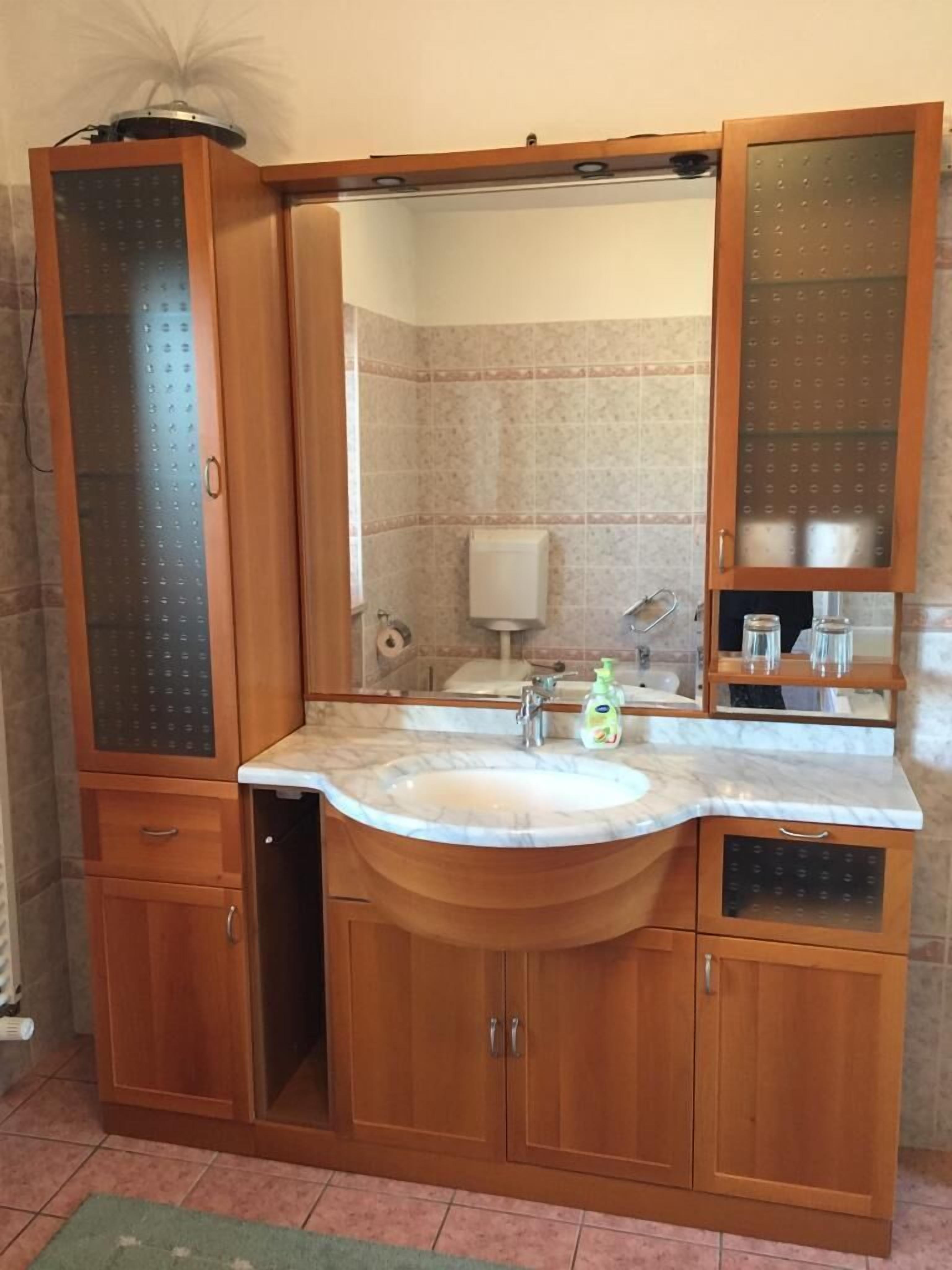 A bathroom with a marble sink, wooden cabinets, a mirror, and a toilet paper dispenser.