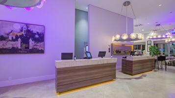 A modern hotel lobby with a reception desk, a bar area, and a large painting on the wall.
