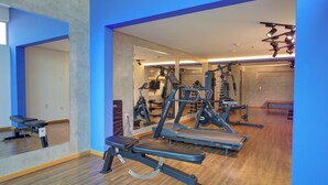 Un gimnasio con equipo de ejercicio, pisos de madera y paredes azules.