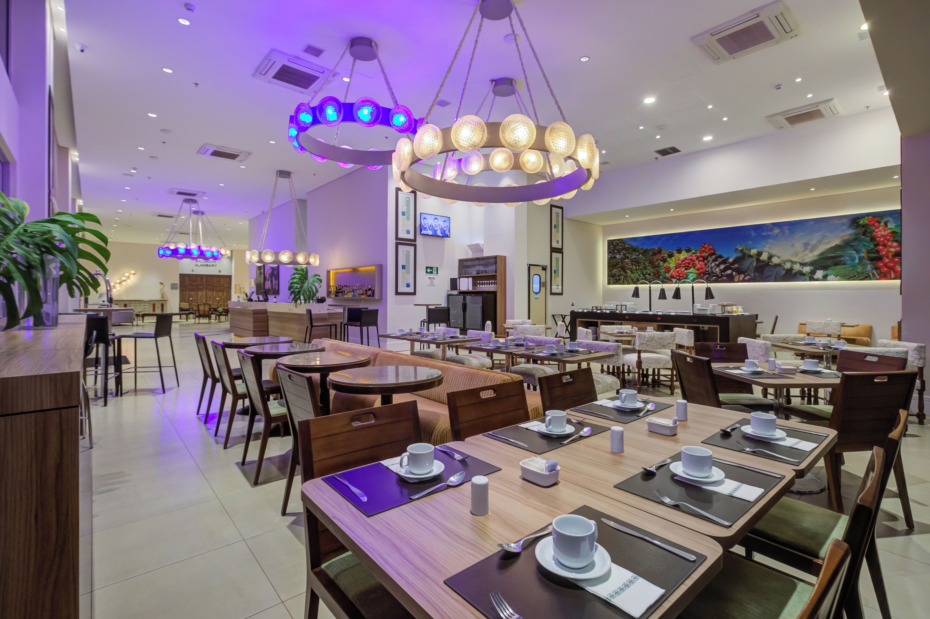 A modern restaurant with multiple dining tables and chairs, ambient lighting, and a large mural on the wall.