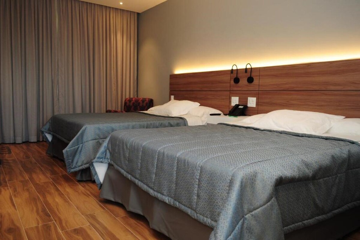 Una habitación de hotel con dos camas, cabeceros de madera y un ventanal con cortinas.