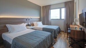 Habitación de hotel con dos camas, un escritorio, un televisor y una ventana con cortinas.