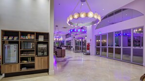 Un vestíbulo amplio con diseño moderno, que cuenta con una zona de estar central, un mostrador de recepción y un gran acceso por puerta de vidrio.