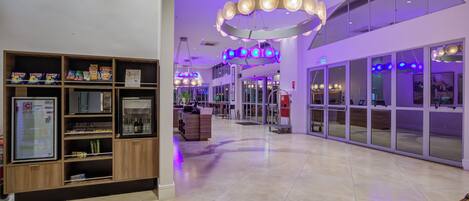 A spacious lobby with a modern design, featuring a central seating area, a reception desk, and a large glass door entrance.