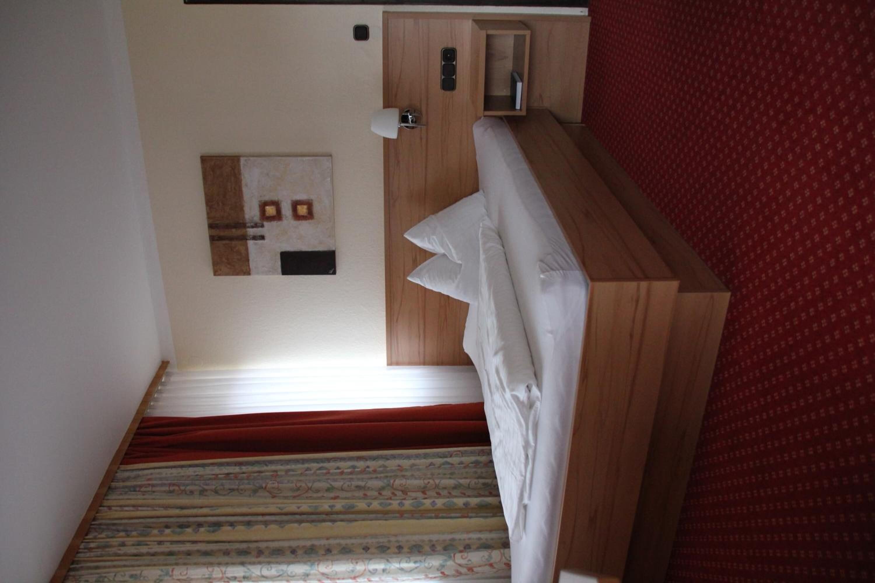 A narrow staircase with patterned carpet leading to a room with a wooden headboard and a red wall.