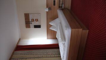 A narrow staircase with patterned carpet leading to a room with a wooden headboard and a red wall.