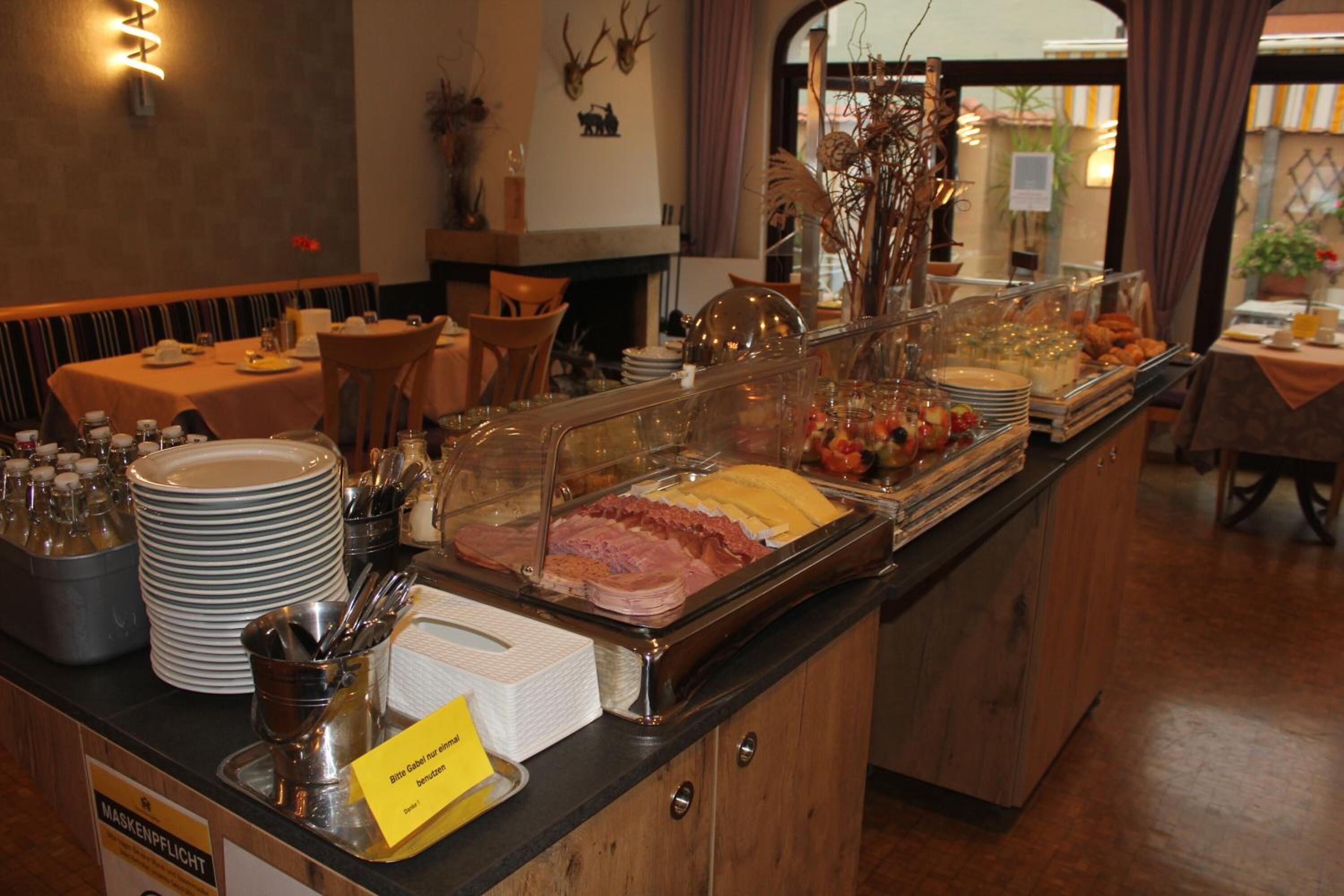 A buffet area with various food items, a sign indicating mask usage, and a wooden counter.