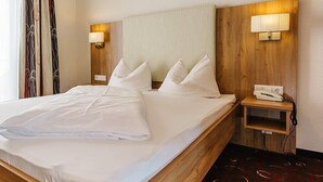 A hotel room with a large bed, two bedside lamps, a wooden headboard, and a small bedside table with a phone. - Hotel Garni Fuchs (Eichstaett)