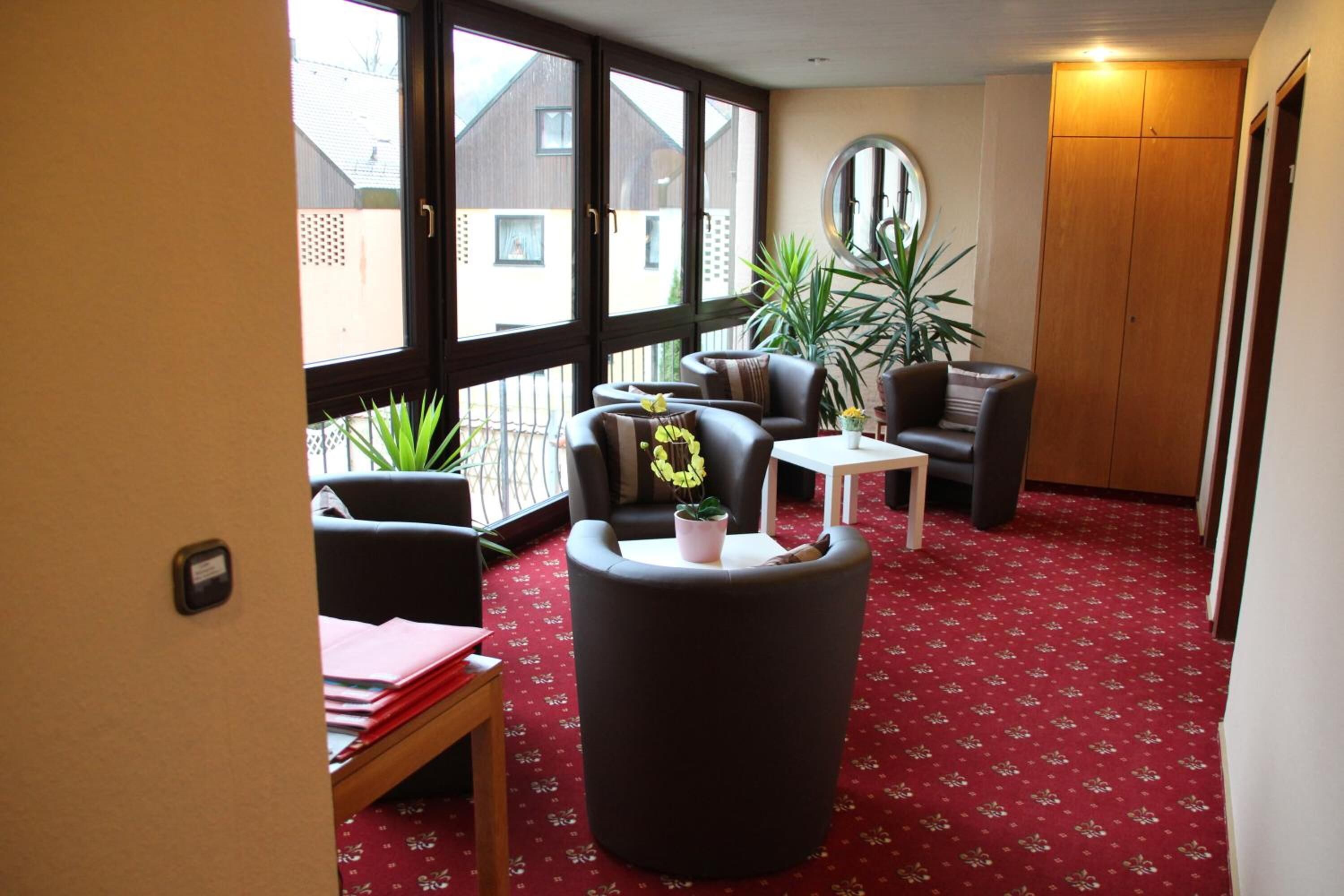 A room with a red carpet, a round mirror, a wooden wardrobe, and a balcony with plants.