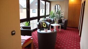 A room with a red carpet, a round mirror, a wooden wardrobe, and a balcony with plants.