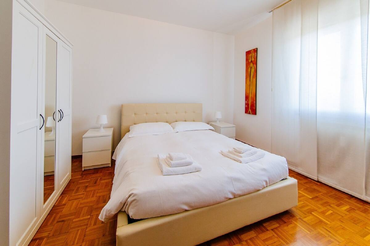 A neatly arranged bedroom with a bed, bedside tables, a wardrobe, and a painting on the wall.