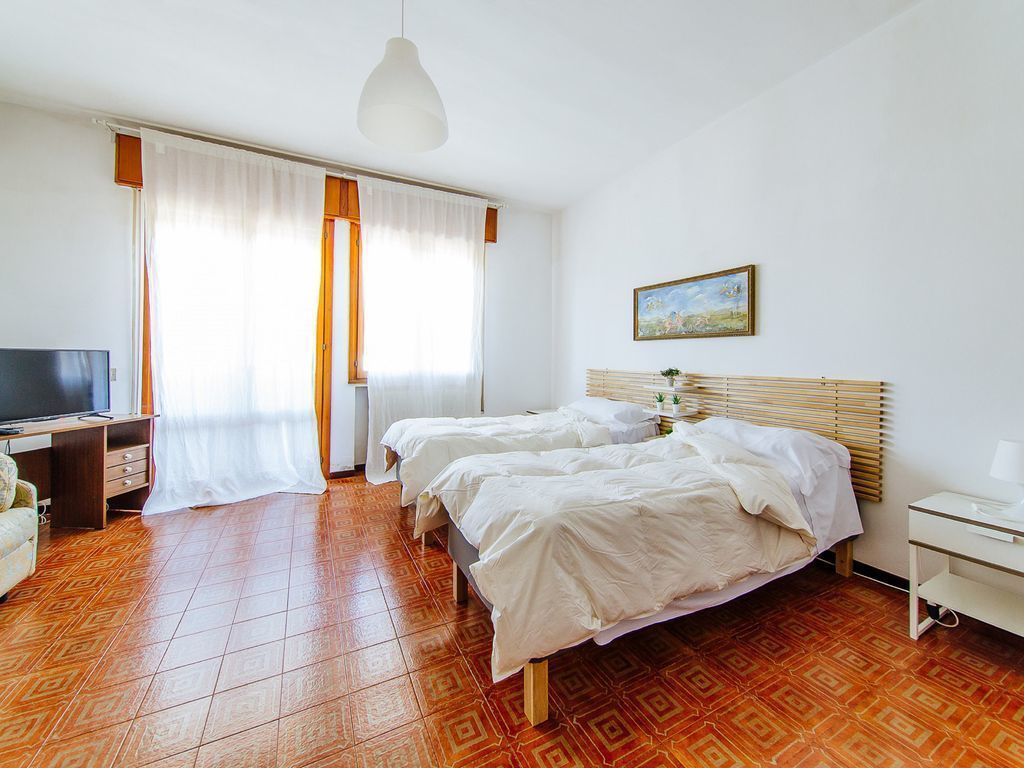 A hotel room with two beds, a desk, a TV, and a window with curtains.