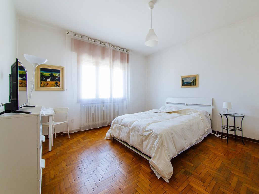 Un dormitorio con cama, escritorio, silla, lámpara y ventana con cortinas.