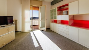 A room with a television, a radiator, a sliding door to a balcony, and a kitchenette with cabinets and drawers. - Welc-oM Manuela (Selvazzano Dentro)