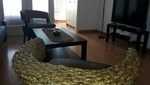 Ett vardagsrum med en flätad stol, ett soffbord, en tv och en lampa.