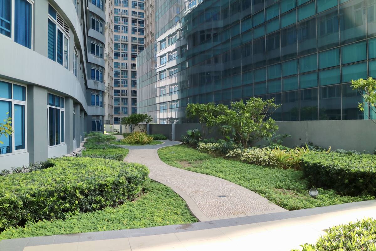 A modern building with a curved glass facade, a landscaped garden with a winding path, and a variety of greenery.