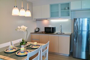 A modern kitchen with a stainless steel refrigerator, a microwave, and a sink. There is a dining table with chairs and a vase of white flowers.