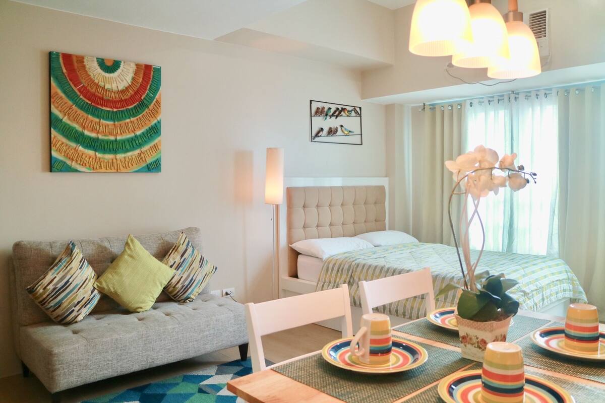 A modern bedroom with a sofa, a bed, a dining table, and a decorative plant.