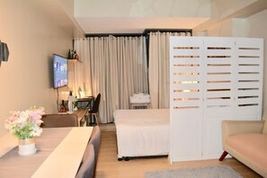 Een hotelkamer met een bed, een bureau met een computer, een televisie en een zithoek met een bank en een fauteuil.