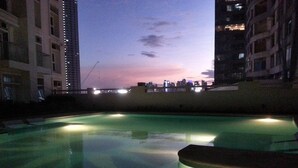 Une piscine avec vue sur le coucher de soleil, entourée d’immeubles de grande hauteur.