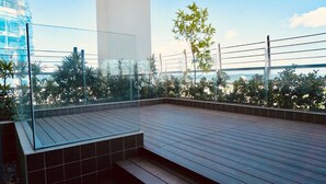 Une terrasse sur le toit, dotée d’une plateforme en bois, d’une rambarde en verre et offrant une vue sur le panorama urbain.