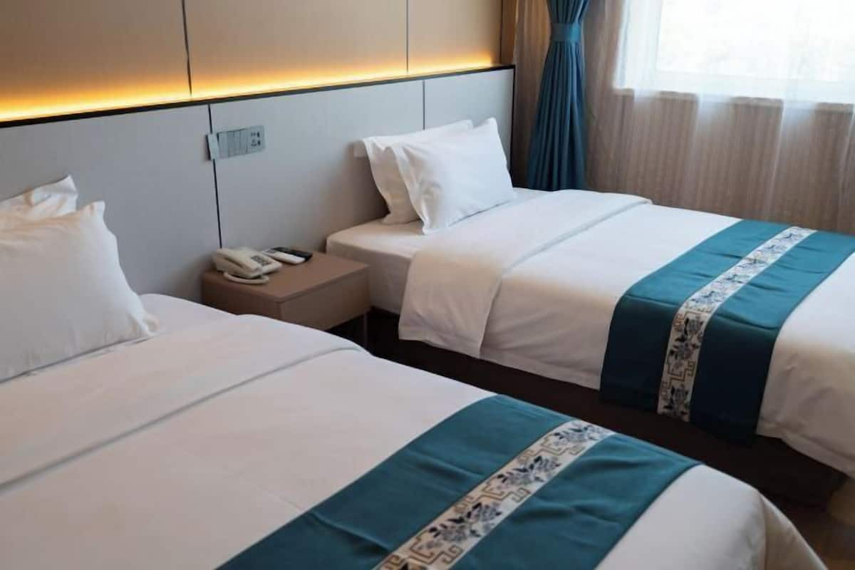 A hotel room with two beds, a bedside table with a phone, and a headboard with built-in lighting.