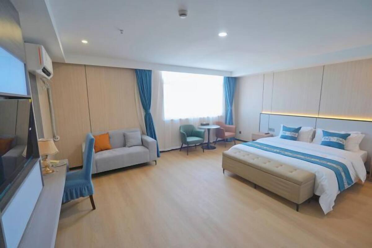 A modern hotel room with a large bed, a sofa, a desk, and a TV.