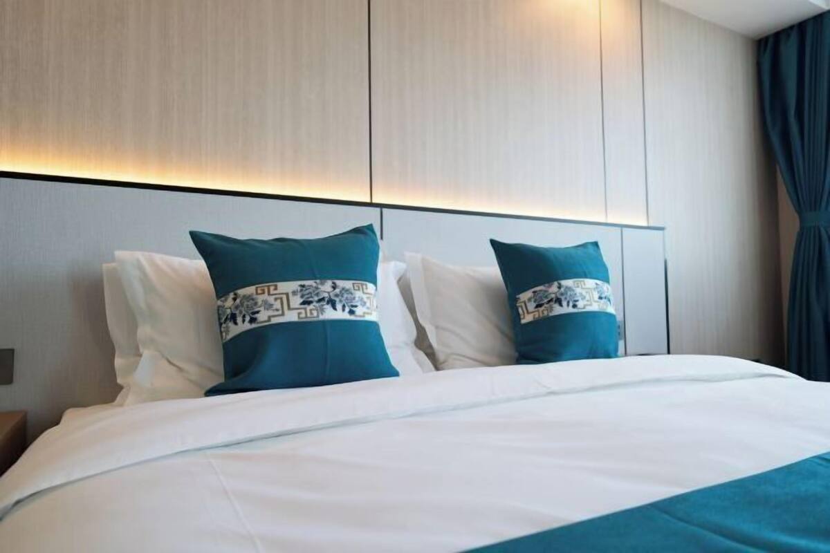 A hotel room with a bed, two decorative pillows, a headboard, and a curtain.